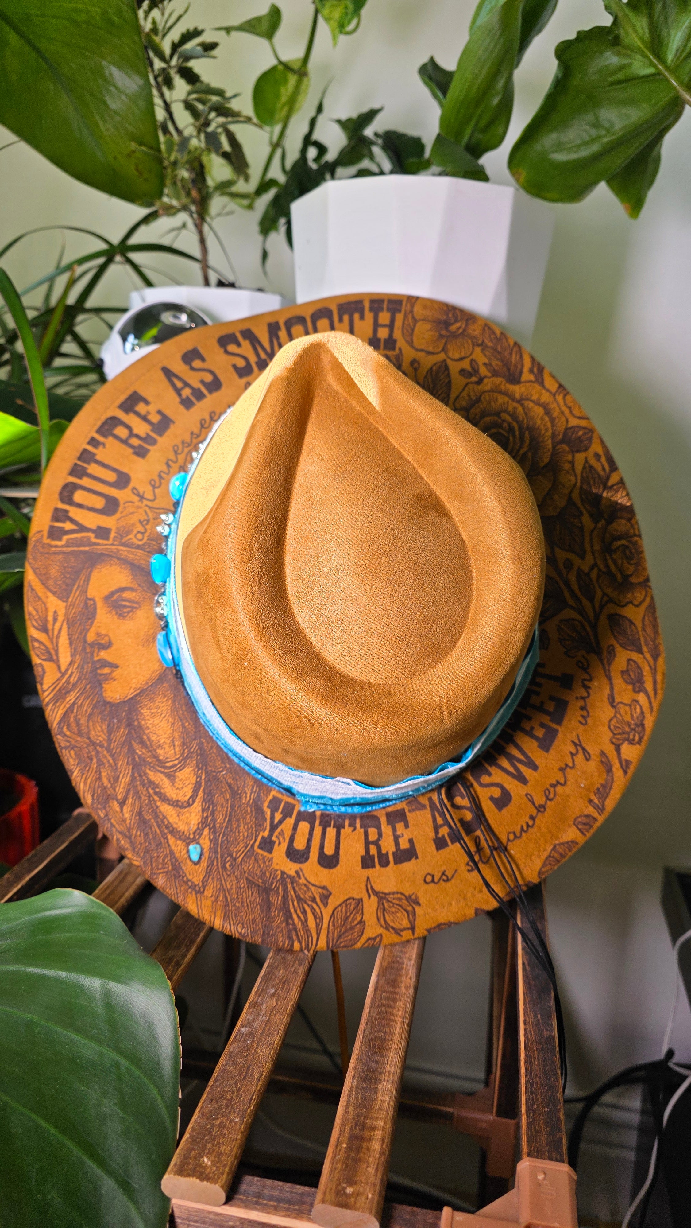 Brown cowboy hat with decorative band on a white surface with green plants in the background